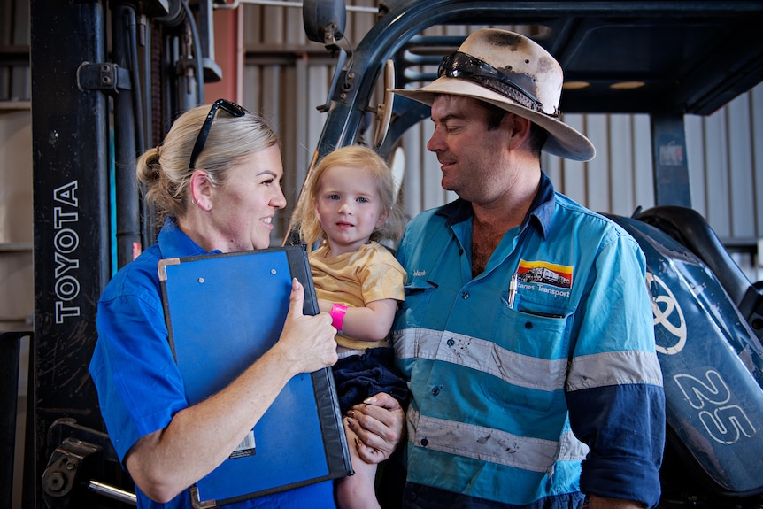 A woman and man look towards a toddler between them.