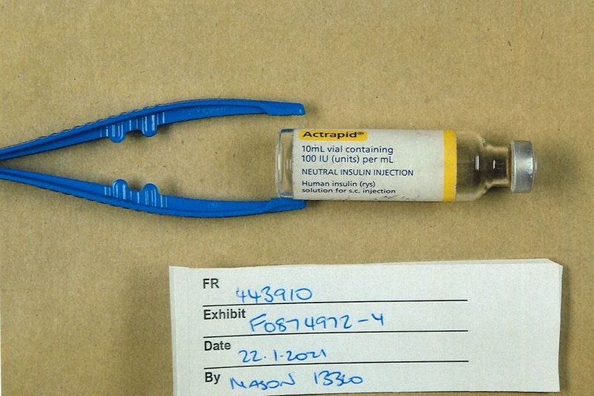 A vial of medicine next to a pair of blue plastic tongs with a label underneath. 