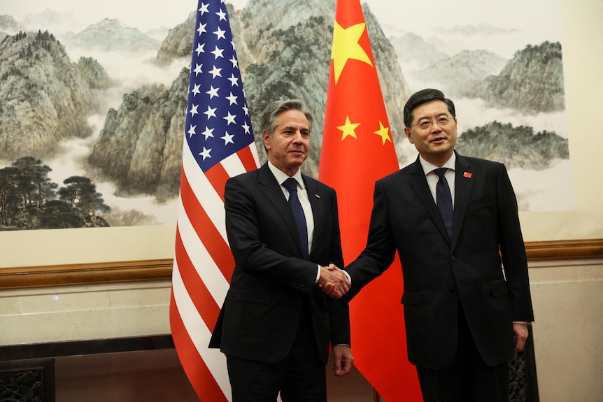 US Secretary of State Antony Blinken shakes hands with China's Foreign Minister Qin Gang with flags of both countries behind. 