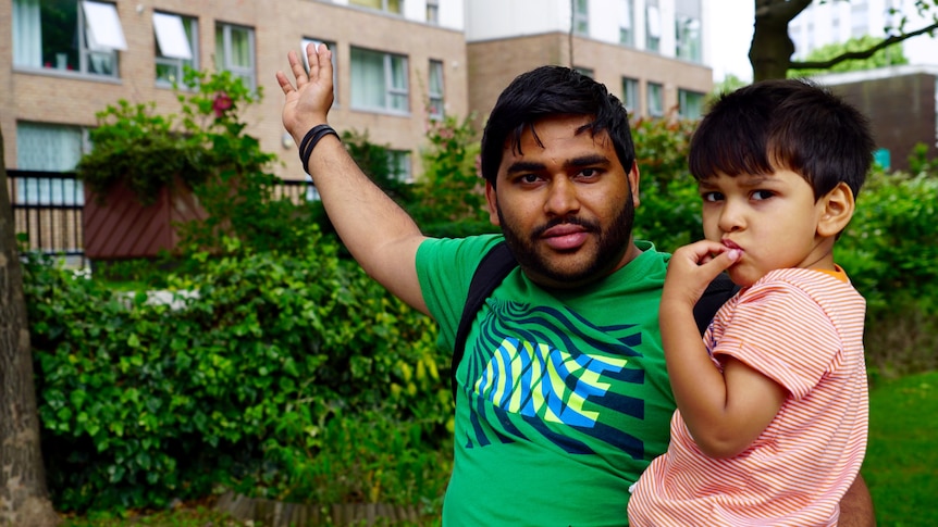 London resident Dominic Reay gestures towards the building behind him while holding his young son.