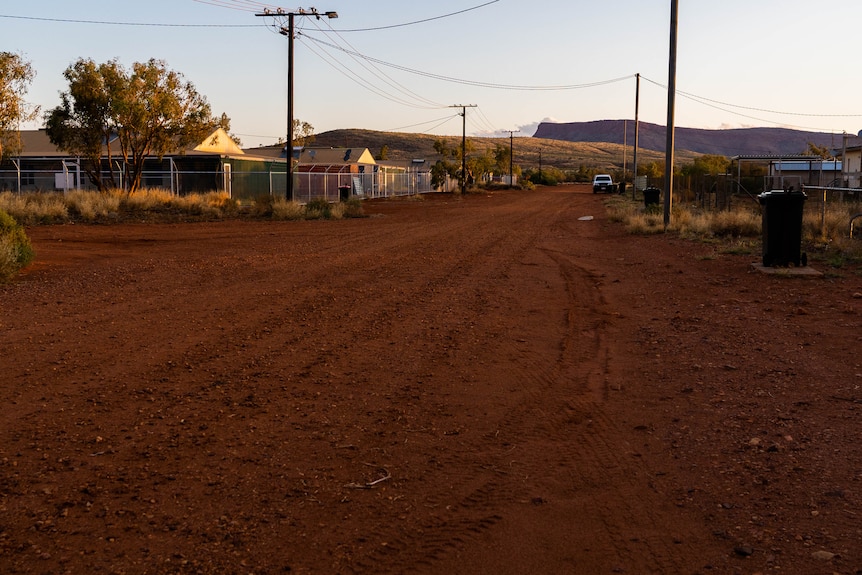 An orange dirt road and houses in remote community.