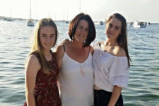 Two girls pose with their mother at a beach for a family photo shoot.