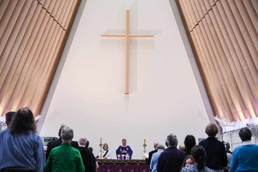 Dean Lawrence Kimberly stands at the altar wearing purple robes. Rows of churchgoers are seen standing in front of him.