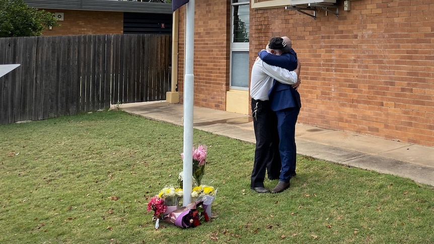 two men hugging next to flowers