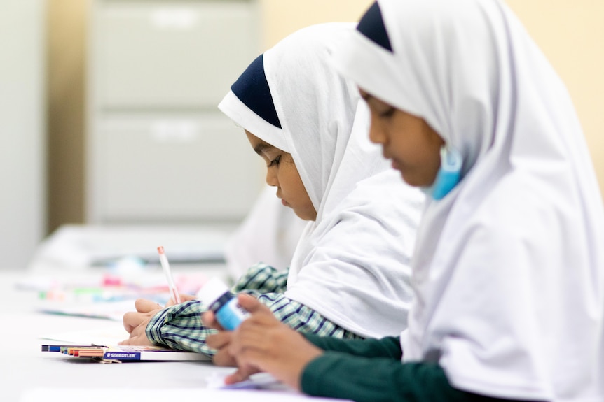 Two students wearing headscarves work in notebooks at a desk.