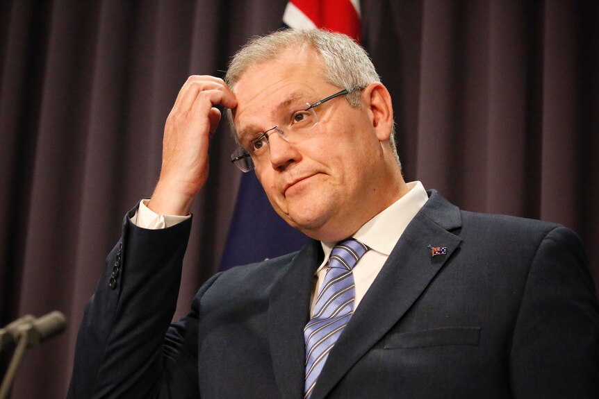 Liberal MP Scott Morrison looks confused and scratches his forehead during a media conference in front of Australian flag.
