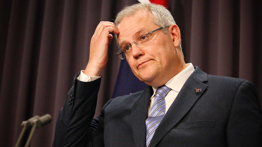 Liberal MP Scott Morrison looks confused and scratches his forehead during a media conference in front of Australian flag.