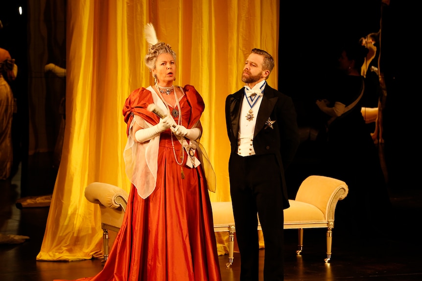 A woman and man on stage  in 19th century garb.