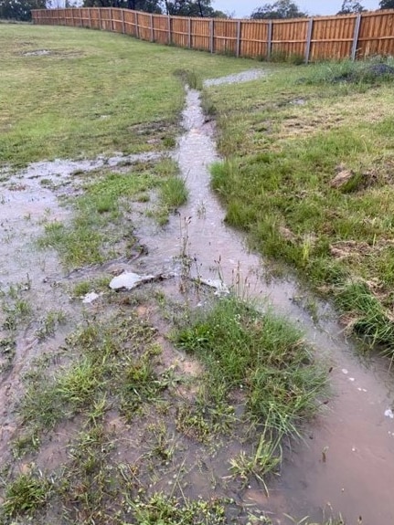 El agua de lluvia corre por una zanja en un patio suburbano.