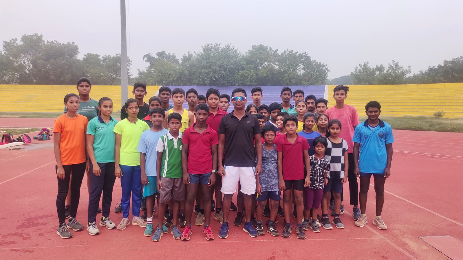 Santhi Soundarajan is surrounded by youth athletes while standing on an athletics track.