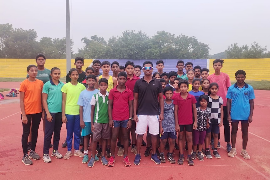 Santhi Soundarajan is surrounded by youth athletes while standing on an athletics track.