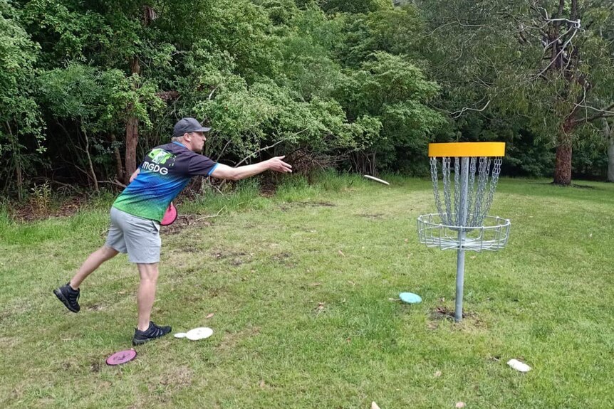 Un hombre lanzando un disco frisbee hacia un objetivo de golf de disco. 