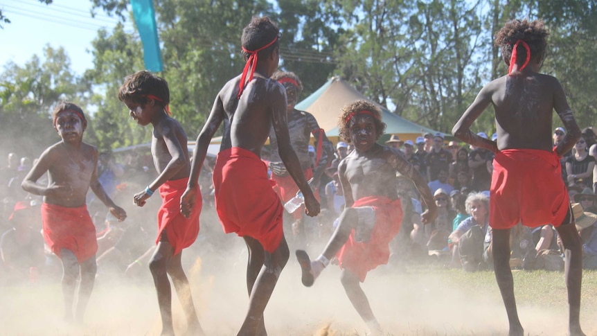 Aboriginal children in red and wearing headbands dance at Barunga