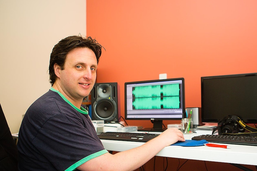 A man looks away from computer screen to camera.