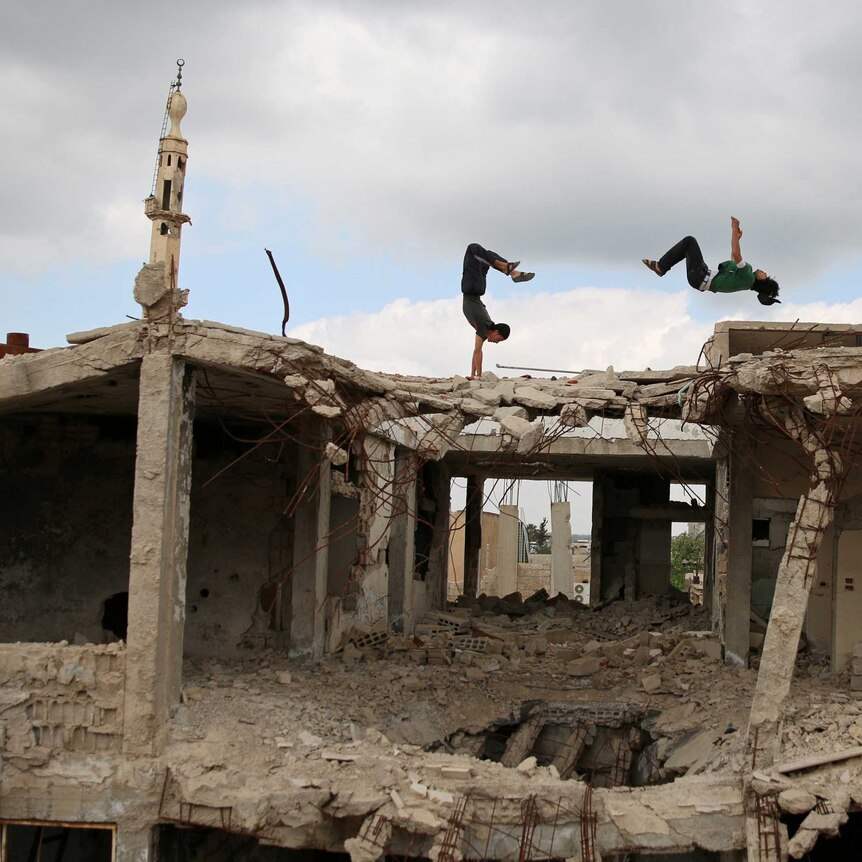 Two Syrian men perform parkour moves on the roof of a mostly-destroyed building in the Syrian city of Inkhil.