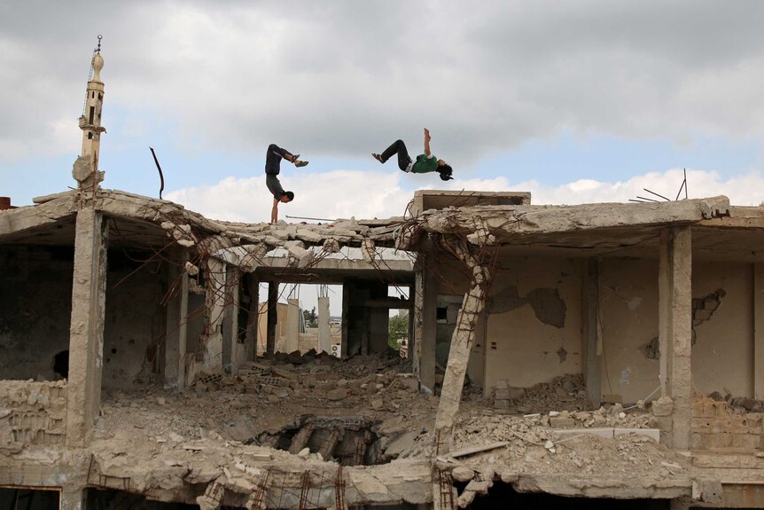 Two Syrian men perform parkour moves on the roof of a mostly-destroyed building in the Syrian city of Inkhil.