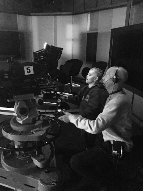 Black and white photo of a man showing a small boy how to look through a studio camera view finder.