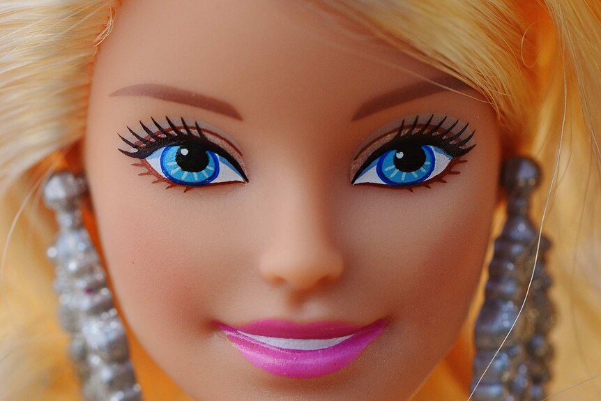 Close up photo of blonde Barbie doll with blue eyes wearing big silver earrings