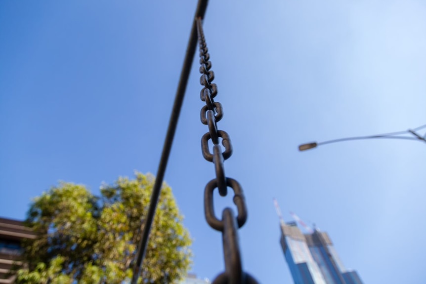 A metal chain stretches up against a blue sky in front of the city skyline.