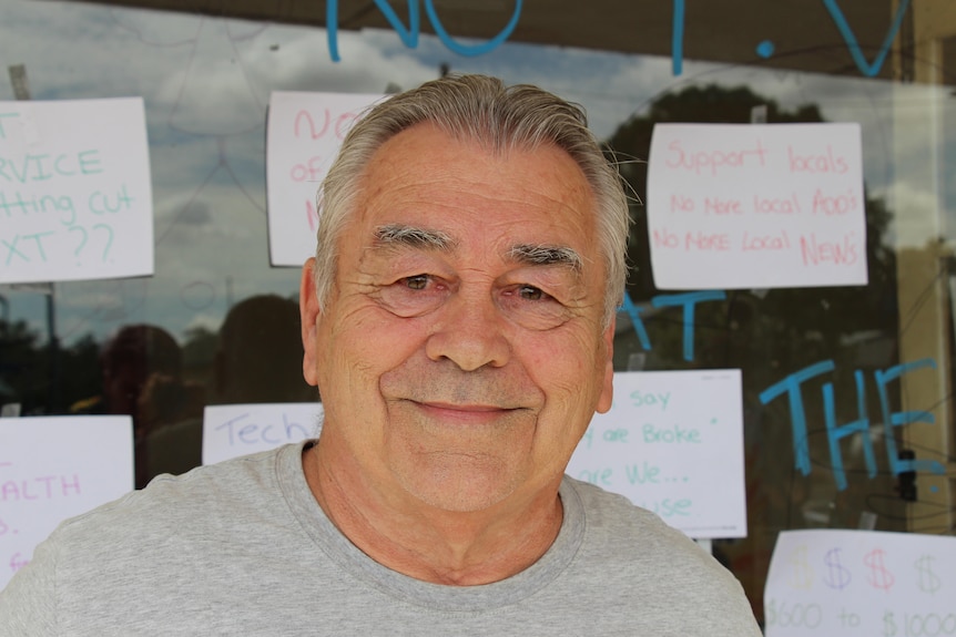 A middle-aged man with grey hair and a grey shirt faces the camera from in front of a window. 