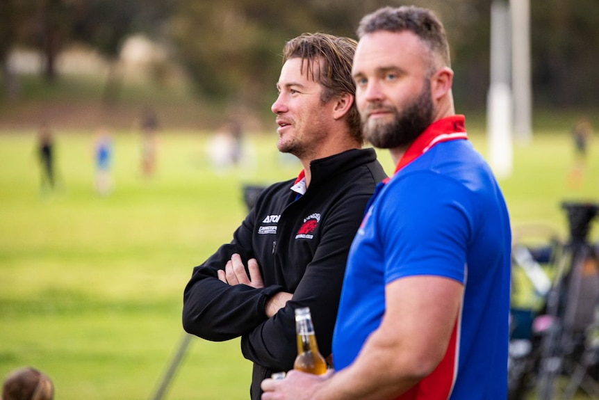 A side shot of Todd standing next to another man and looking at the field   