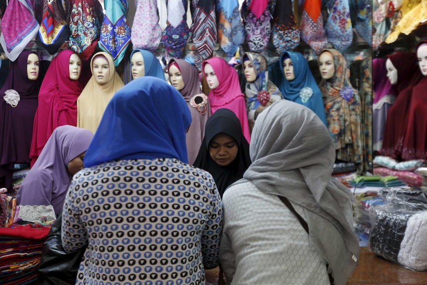 Two women wearing hijabs stand in front of a counter where they are served by another woman at a hijab shop