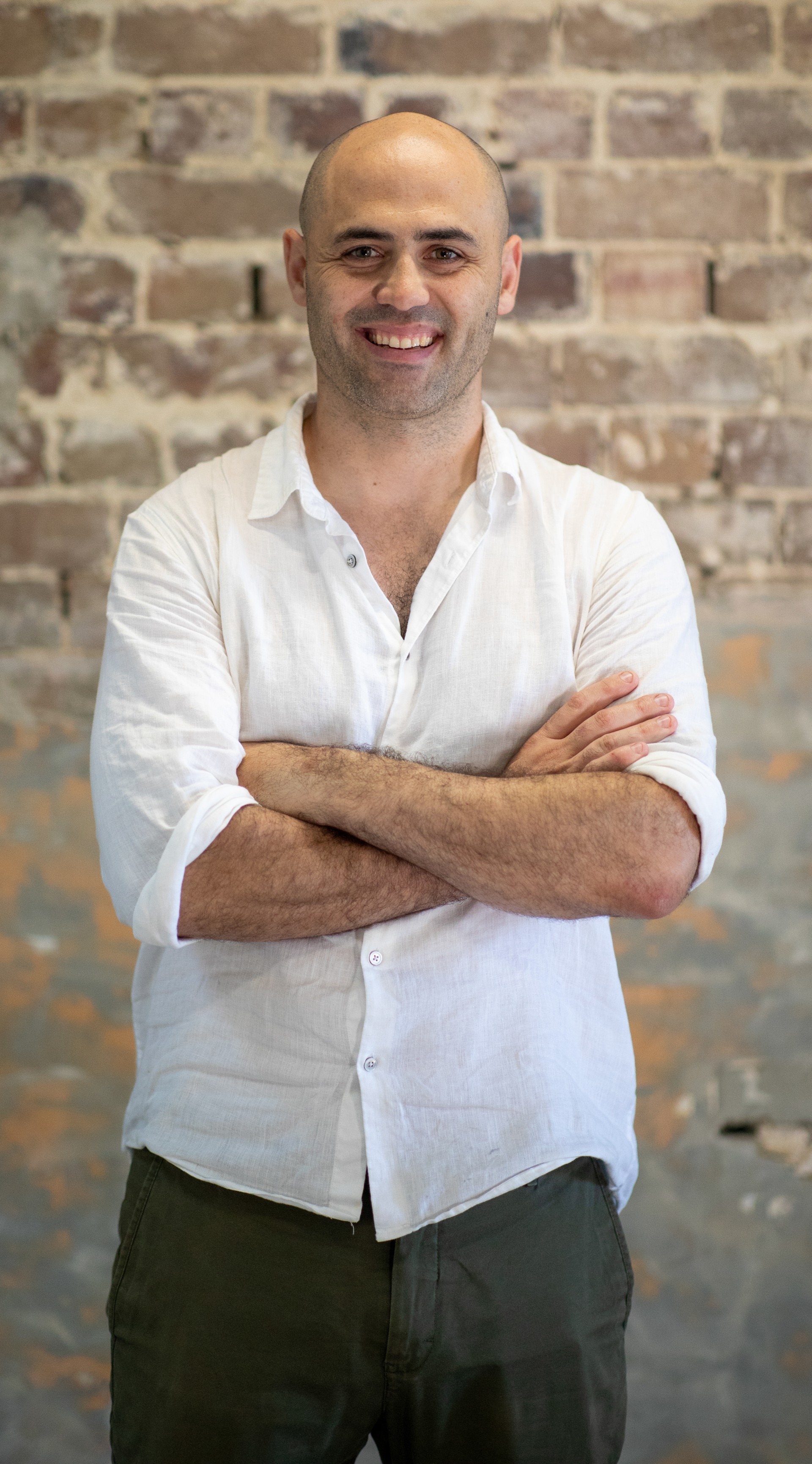 man in a white shirt crosses his arms in front of a brick wall