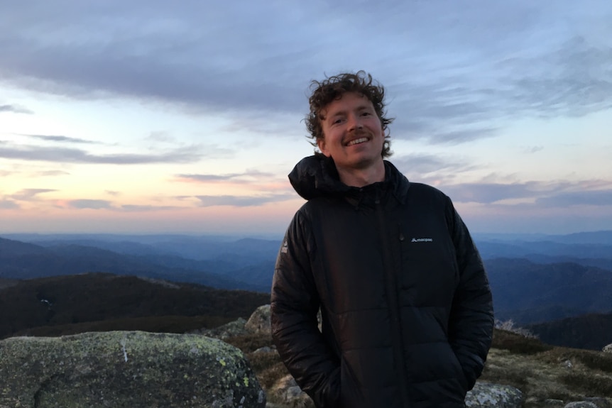 man on a mountain with sunrise behind him smiling