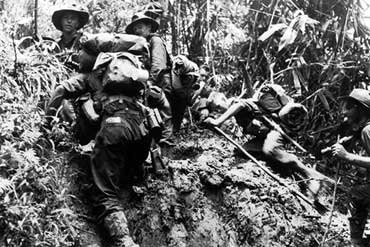 Soldiers climbing muddy Kokoda track.