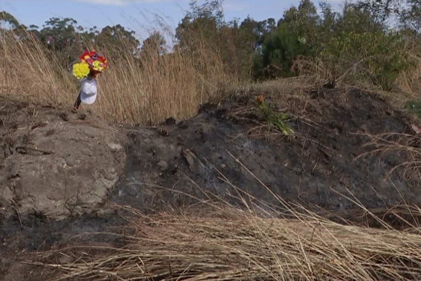 A flower tribute sits on top of a pile of burnt earth.