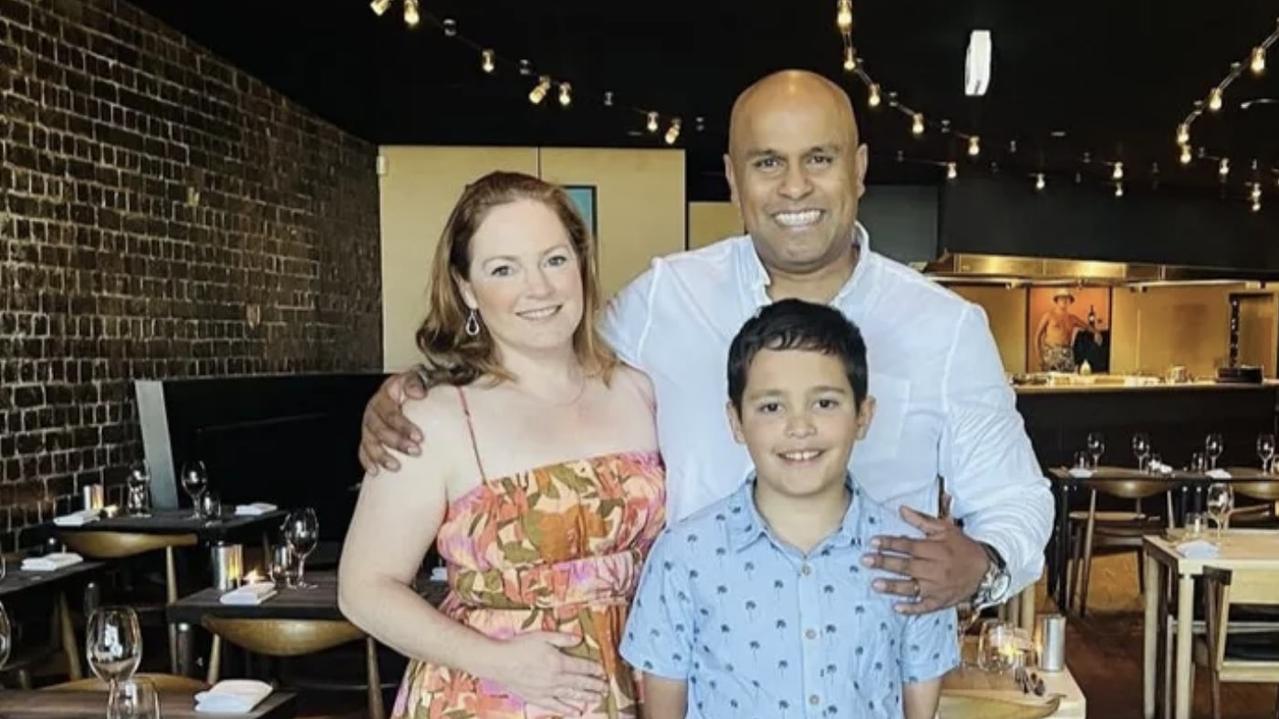 The family stands in a restaurant with Raj holding his arm around Emma's shoulder and his other hand on Arli's shoulder.
