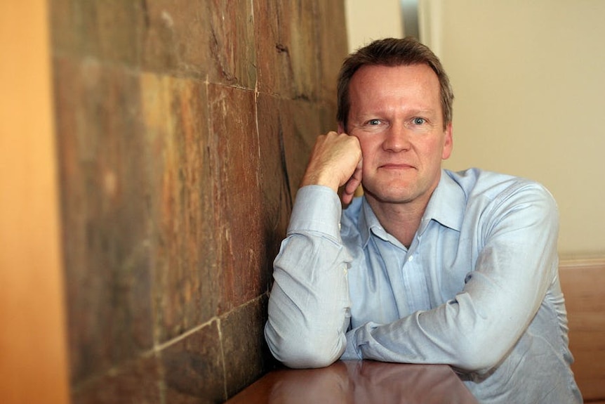 Pasi Sahlberg leaning on a bench with his head resting on his hand.