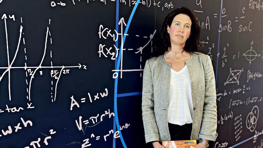 A female teacher standing in front of a wall decorated with a maths equation