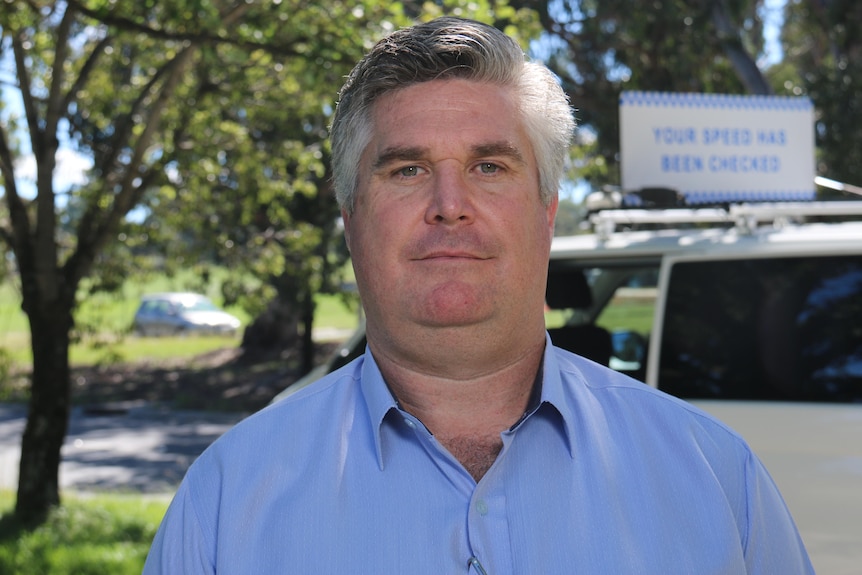 A man looks at the camera with a speeding sign in the background.