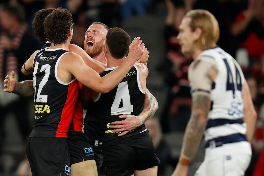 St Kilda players join in a tight hug with a sad Geelong player in front of them