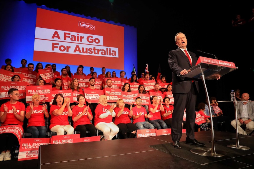 Bill shorten speaks at a lectern with supporters behind him