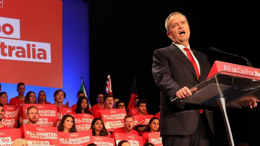 Bill shorten speaks at a lectern with supporters behind him