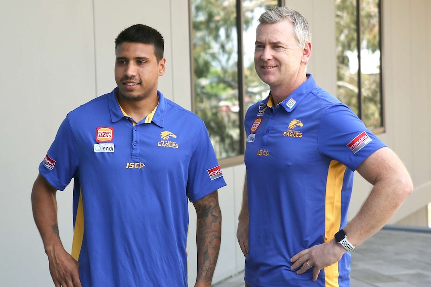 Tim Kelly stands next to Adam Simpson with both men smiling and wearing blue West Coast Eagles shirts.