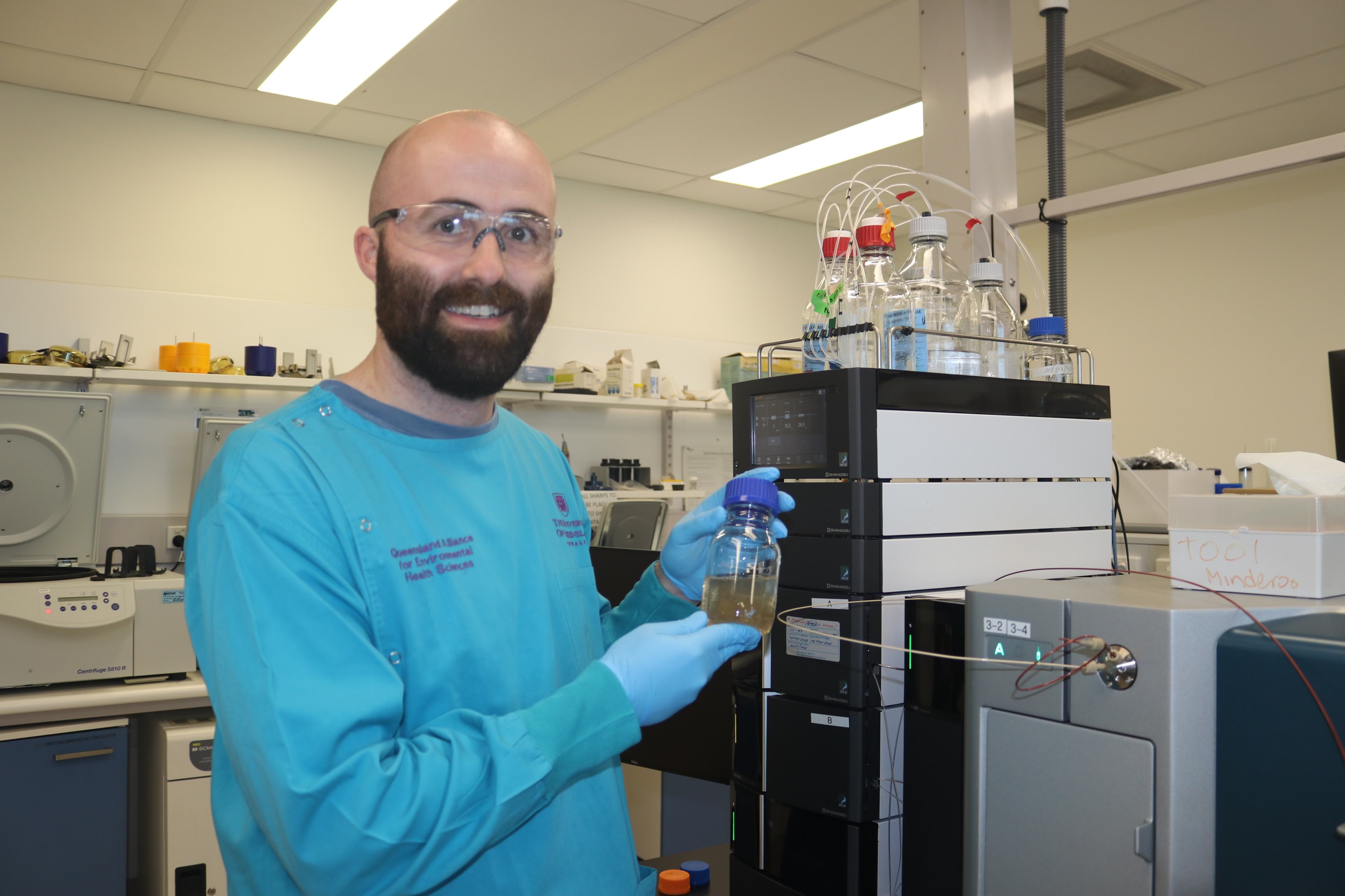 An image of Dr Rory Verhagen holding a test tube of wastewater wearing scrubs