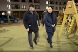 Vladimir Putin wears a winter puffer jacket as he walks along a city street at night with a man