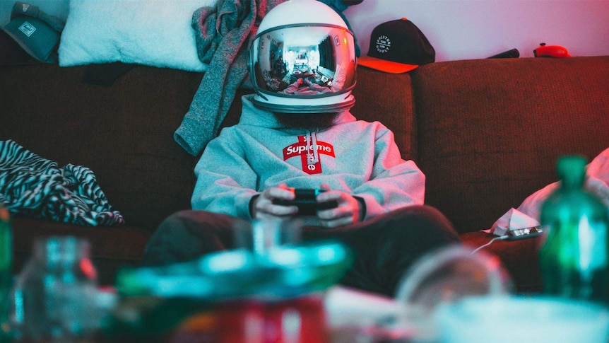 A man wits on a couch with a helmet on and playing a video game