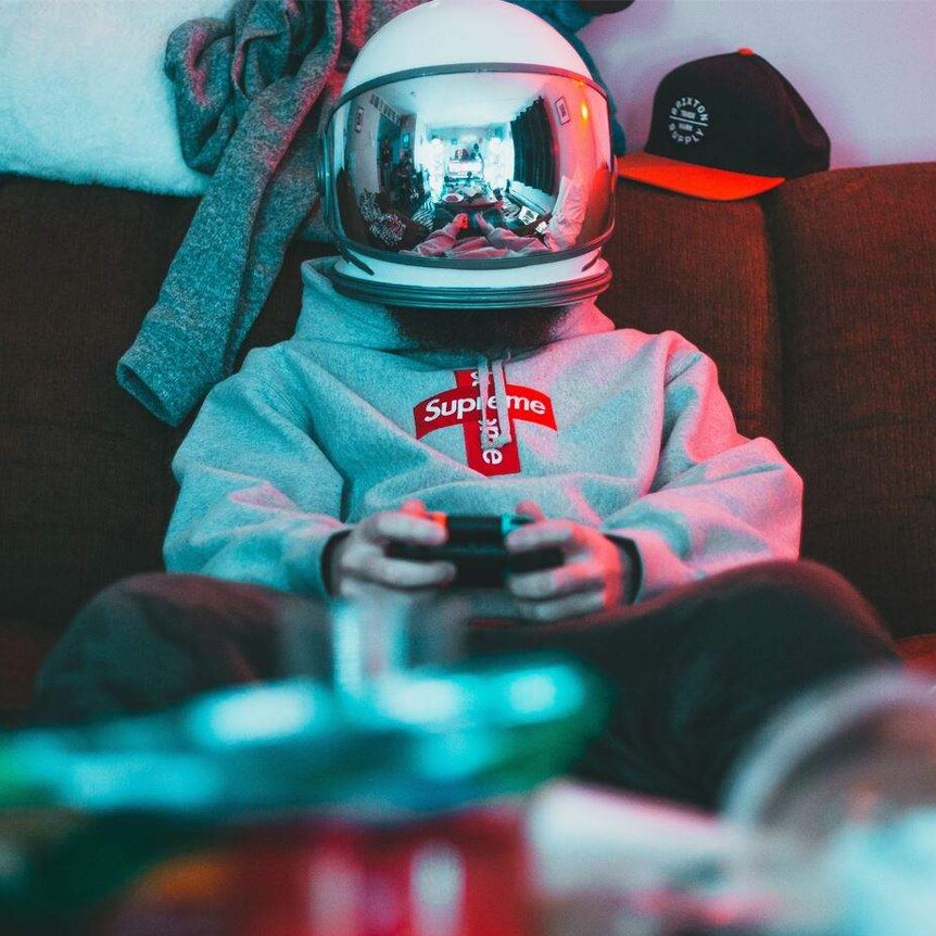 A man wits on a couch with a helmet on and playing a video game