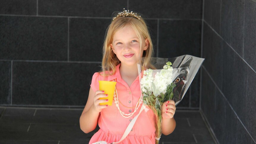 A young girl wearing a tiara holds a bunch of flowers while waiting for the royal arrival