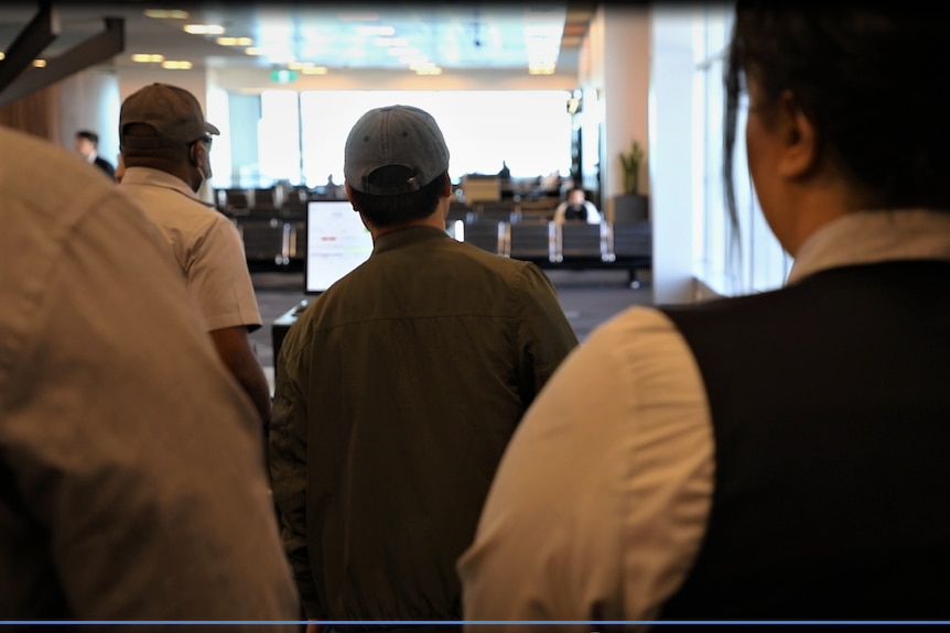 The back of the head of a man who is being escorted through an airport.