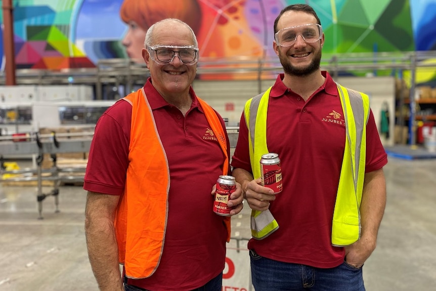 Two men standing next to each other with a beer cans in their hands.