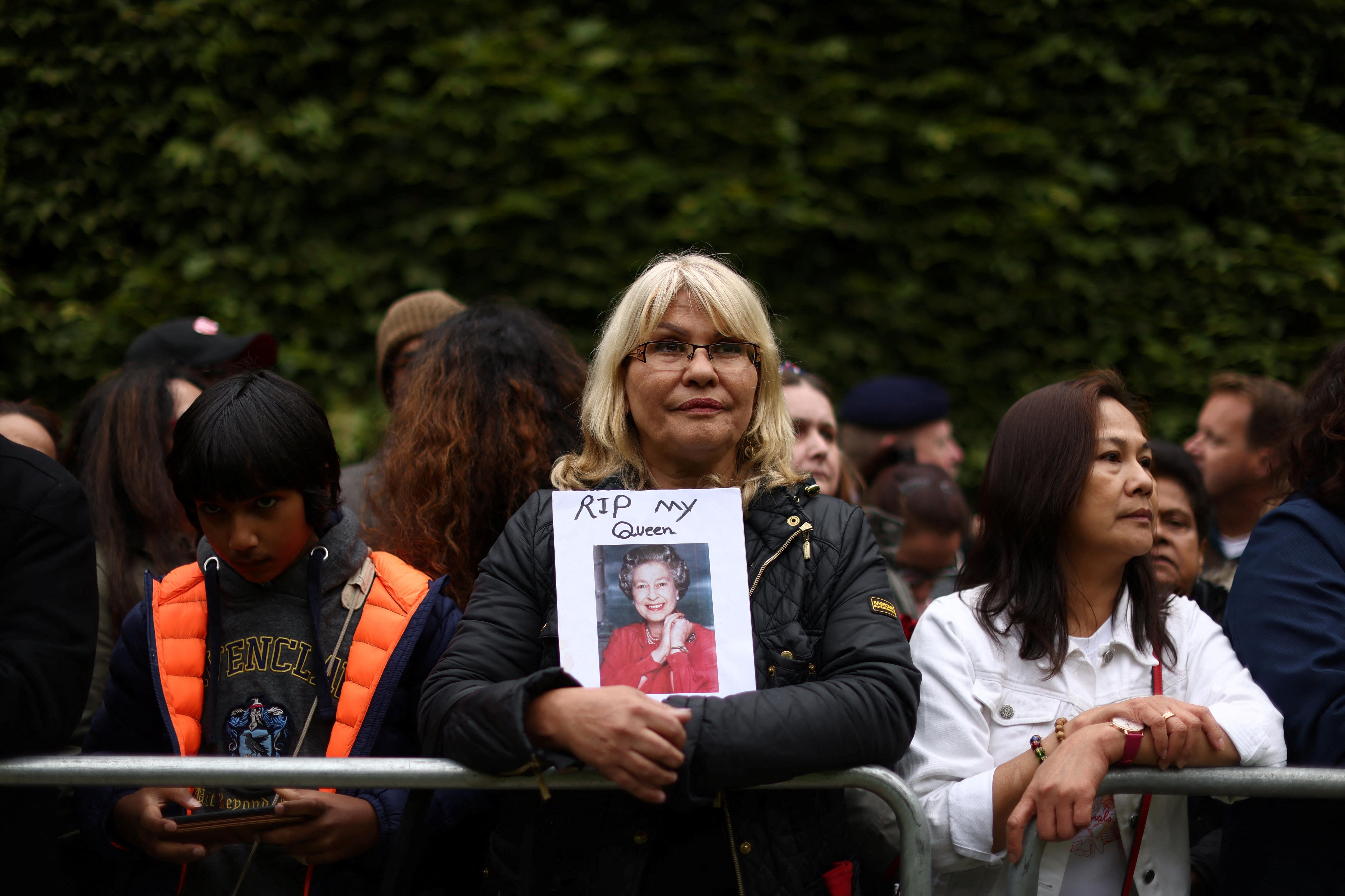 A woman standing in the crowd holds a portrait of the queen with RIP My Queen written on it. 