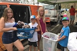 A woman with three children stand in front of an orange van holding baskets of clean clothes