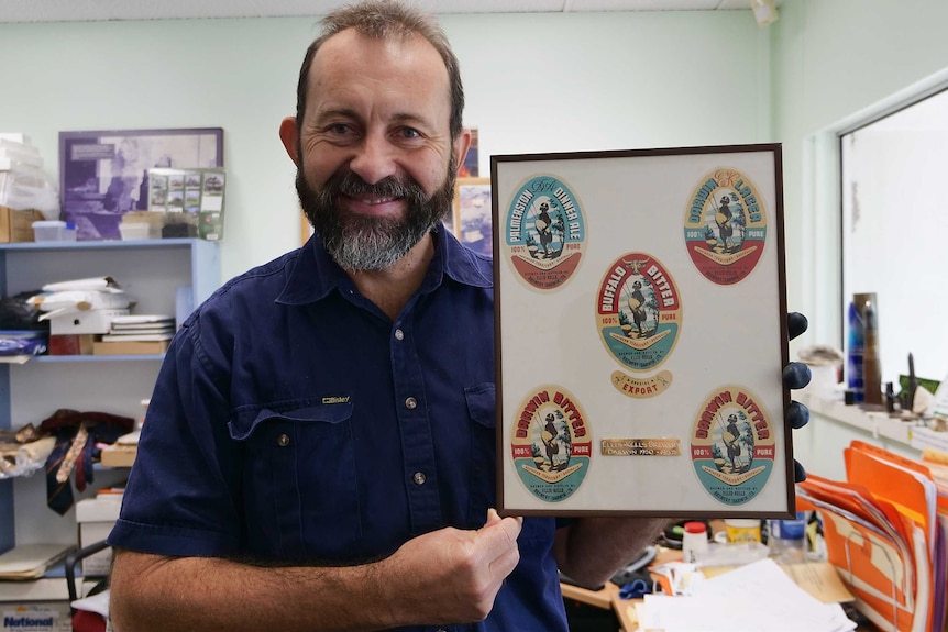 A man holds up framed beer labels in a Northern Territory museum