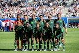 A women's soccer team wearing dark green poses for a photo before a big game