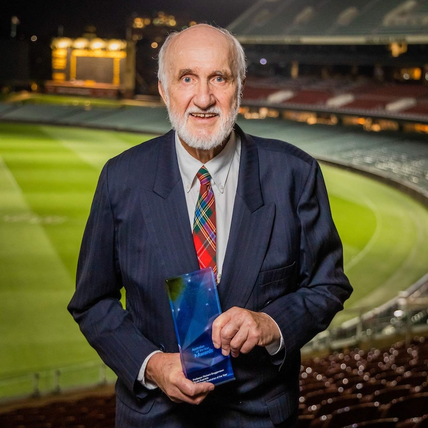 A man with a white beard and bald head wearing a suit and holding an award